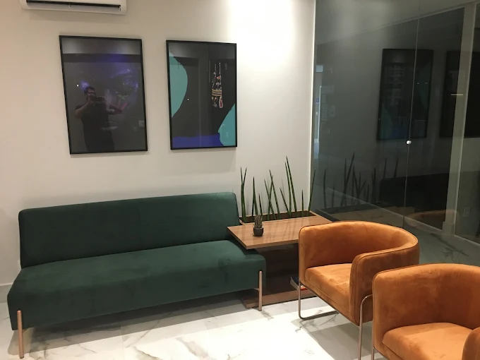 Espaço de espera com sofá verde e poltronas em tom terracota